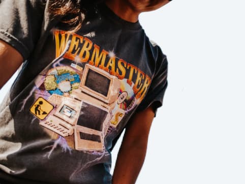 A person wearing a t-shirt that has graphics of 90s era computer gear and has the text Webmaster